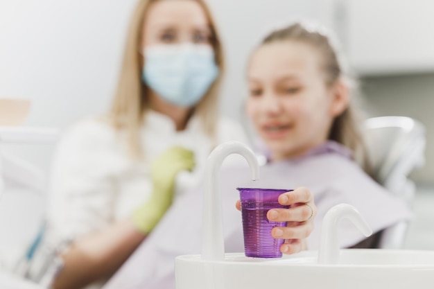 치과에서 구강 세척제를 위한 일회용 물 컵을 들고 있는 십대 소녀의 클로즈업.