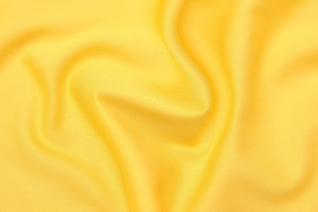 Close-up texture of natural orange or yellow fabric or cloth in same color. Fabric texture of natural cotton, silk or wool, or linen textile material. Yellow canvas background.