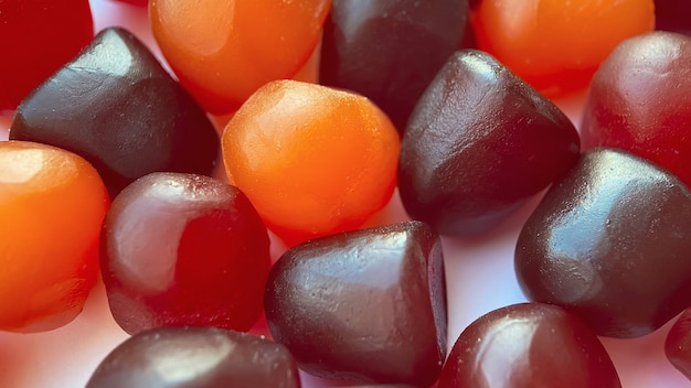 Texture ravvicinata di caramelle gommose multivitaminiche rosse, arancioni e viola su sfondo bianco. concetto di stile di vita sano.
