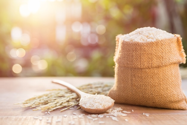 Close up Thai jasmine rice in small sack on wooden table with sunlight blur