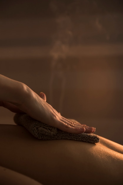 Close-up of a therapist hand massaging woman's back with hot towel