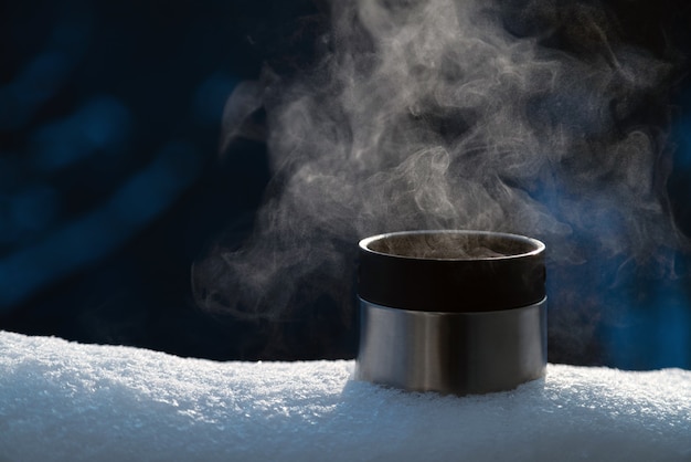 Close up of thermos cup with hot steaming drink outside on the snow. Nobody