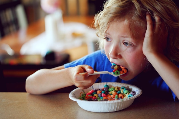 Foto close-up di un ragazzo riflessivo che mangia cereali da colazione multicolori sul tavolo