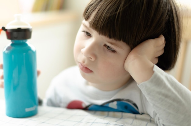 close-up of thoughtful boy sitting with bottle at table