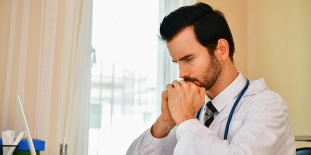 Photo close-up of thoughtful male doctor sitting in clinic