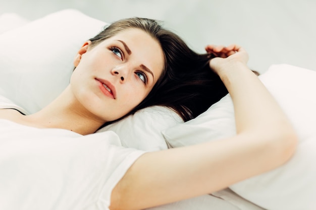 家でベッドに横たわっている思慮深い若い女性のクローズアップ