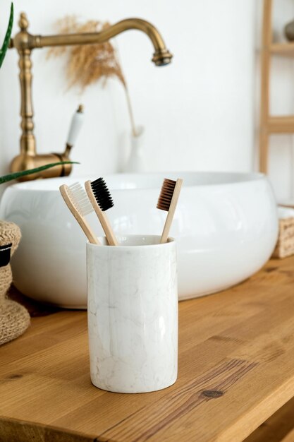 Photo close up of three bamboo toothbrushes in a glass on wooden table in bathroom