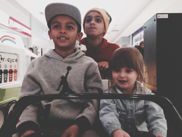 Photo close-up of three children sitting in toy car