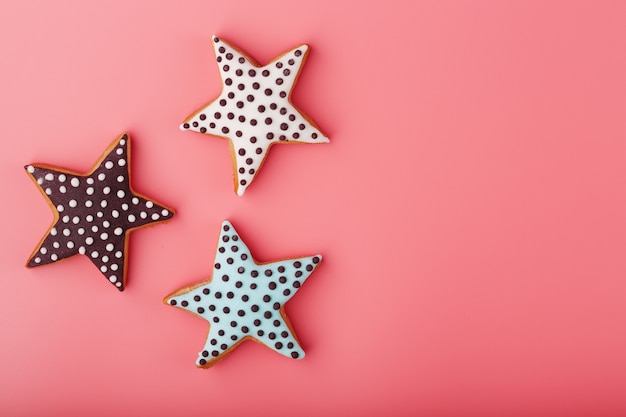 Foto un primo piano di tre biscotti di panpepato smaltati fatti in casa è fatto sotto forma di stelle su uno sfondo rosa. biscotti fatti a mano.