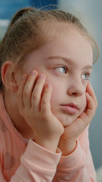 Close up of tired child listening to remote online lesson for school work at home. Exhausted young girl looking at screen for learning and class tasks while sitting at desk, falling asleep