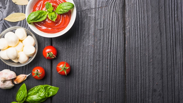 Photo close-up of tomato sauce with mozzarella; pasta; garlic an basil on wooden plank