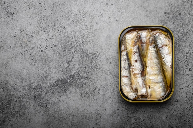 Close up and top view of canned sardine in a tin over gray concrete background, space for text. Tinned fish as a convenient, fast, healthy food and source of omega-3 fatty acids, protein and vitamin D
