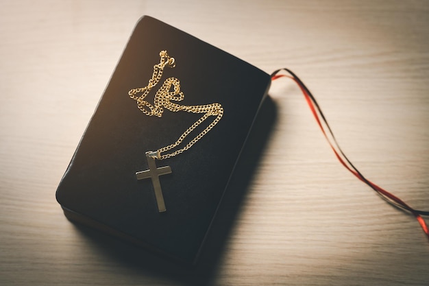 Close up top view Christian gold stainless steel crucifix necklace crosses placed on bible black leather cover place on a wooden table Spirituality and religion Christian prayer religion concept
