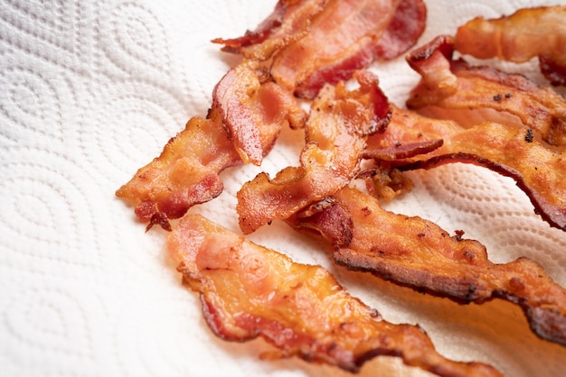 Close up top view of crispy bacon strips on oilabsorbing tissue\
paper in many shapes keto food