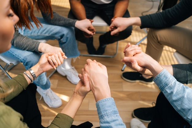 Close-up top view of group diverse multiethnic people holding hands together during the psychological therapy, meditating and solving together mental problems. Concept of consulting of mental problem