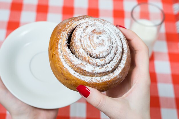 Close up, top view photo of tasty sugary cinnamon roll in woman's hand