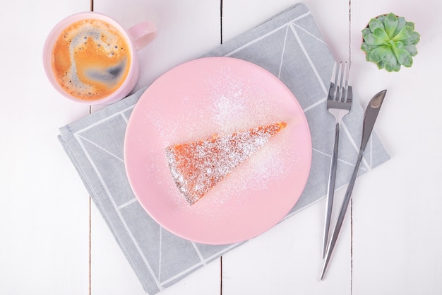 Крупным планом вид сверху кусок пирога на розовой тарелке с ножом и вилкой на сложенной льняной салфетке с геометрическим узором и кружка с кофе. Домашняя выпечка. Выборочный фокус.
