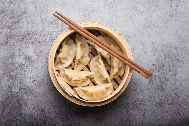 Close-up, top view of traditional Asian/Chinese dumplings in bamboo steamer with chopsticks on gray rustic stone background. Authentic Chinese cuisine