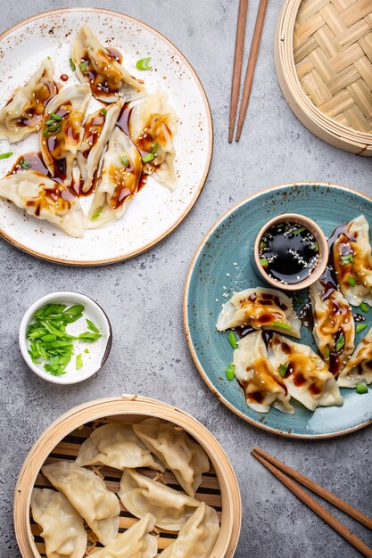 Photo close-up, top view of two plates with traditional asian/chinese dumplings with soy sauce and chopsticks on gray rustic stone background. authentic chinese cuisine