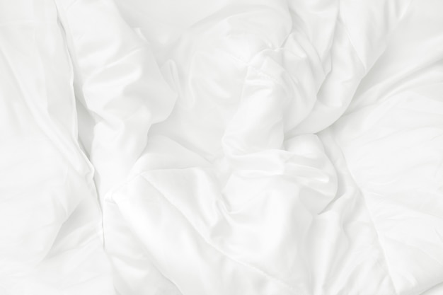 Chiuda sulla vista superiore dello strato della lettiera bianca e della coperta sudicia della grinza in camera da letto.