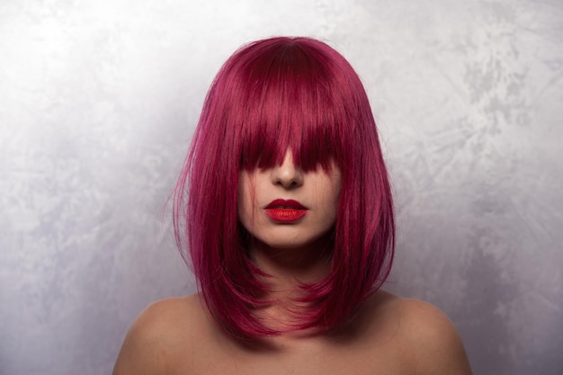 close-up of topless young woman with pink hair standing against wall