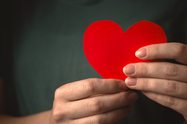 Close-up tot rood hart in handen. Vrouw met papieren hart op haar borst achtergrond