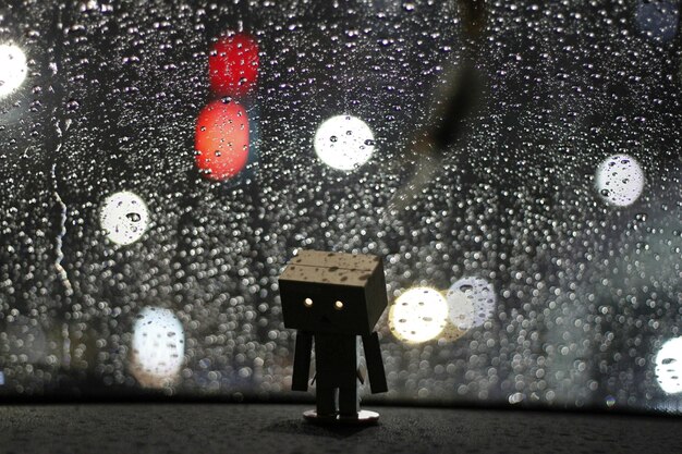 Close-up of toy robot against wet window in rainy season