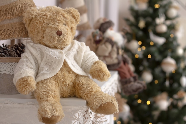 Photo close-up toy teddy bear on a mantelpiece on a blurred background of a decorated christmas tree.