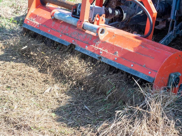 Close-up of a tractor with a chain mower chopping dry grass. Maintenance of the territory, mulching of grass, agricultural machinery.