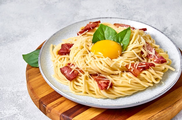 明るい背景のプレートにベーコン、チーズ、卵黄と伝統的なイタリアのパスタカルボナーラを閉じます。