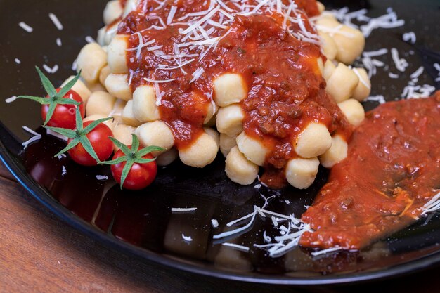 Foto primo piano sugli gnocchi di patate italiani tradizionali in salsa di pomodoro con basilico fresco e pomodoro ciliegino