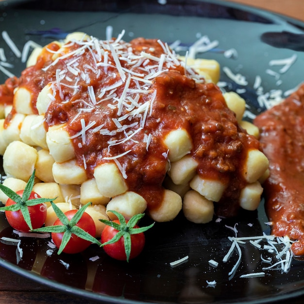 Foto primo piano sugli gnocchi di patate italiani tradizionali in salsa di pomodoro con basilico fresco e pomodoro ciliegino