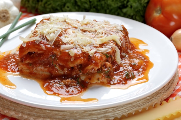 Close-up of a traditional lasagna made with minced beef bolognese sauce topped with basil leafs served on a white plate.