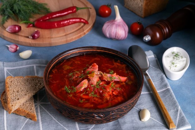 Close-up of the traditional Russian soup borscht made from cabbage, beets and other vegetables served in a clay ceramic plate with sour cream and garlic. National cuisine concept. Selective focus.