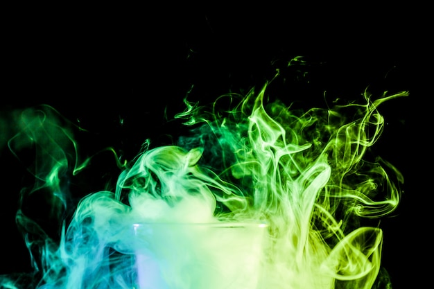 Close up of a  transparent  glass filled with a cloud from a green vape smokes and stands on a black isolated background