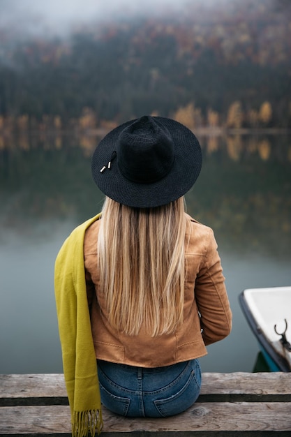 close up of traveler female sitting on a pier near the wilderness forest in autumn season
