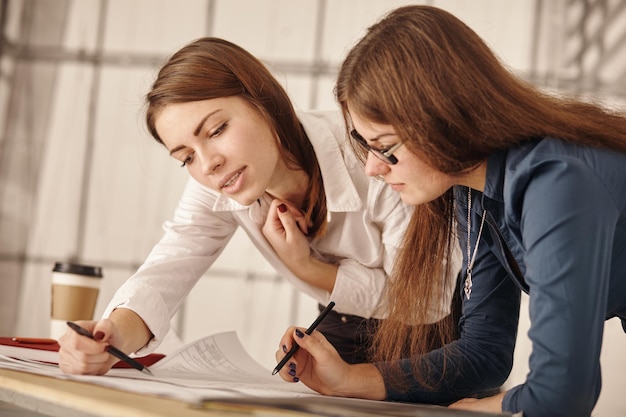 Close-up twee gelukkige jonge zakenvrouwen op kantoor praten over zakelijk verslag op papier.