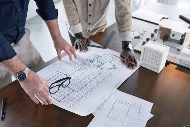 Close-up of two architects drawing blueprint on new project together at the table and discussing it