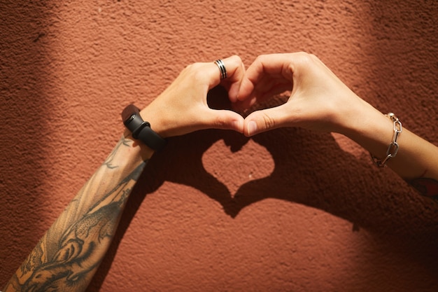 Close-up of two girlfriends making heart shape from their hands against the wall