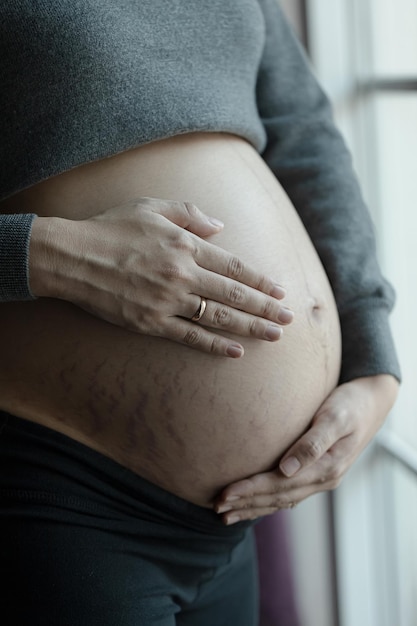 Close up of two hands wearing wedding rings on pregnant woman touching her big belly