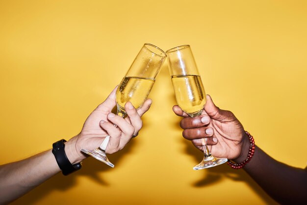 Close up of two people clinking champagne glasses against yellow