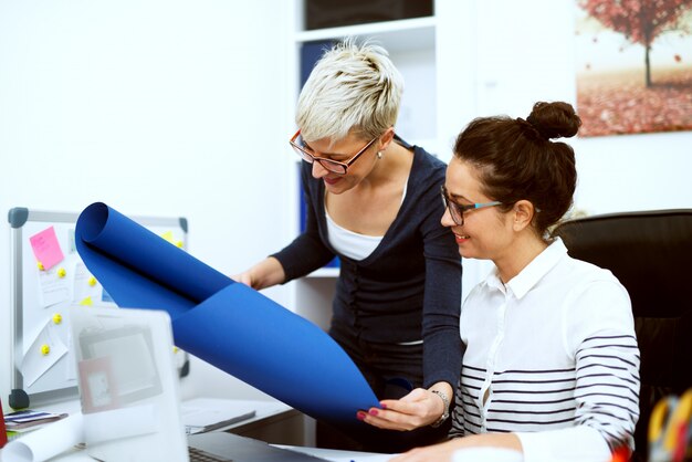 Foto primo piano di due donne di mezza età sorridenti concentrate affari alla moda che lavorano insieme al progetto in ufficio.