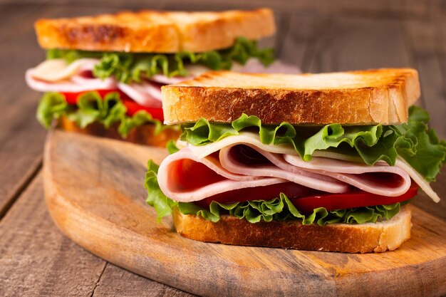 Close-up of two toasted sandwiches with fresh ham, cheese and vegetables on background.