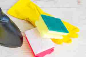 Photo close up of twoo clening sponges yellow rubber gloves and black plastic spray bottle of detergent on wooden background