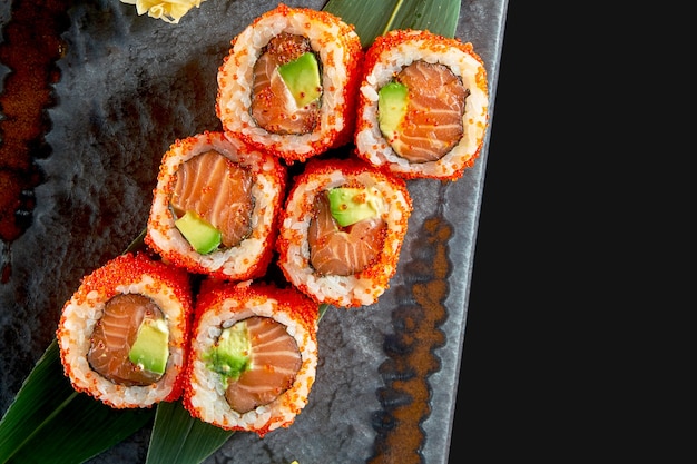 Close-up uitzicht op smakelijke uramaki met zalm, avocado en tobiko kaviaar. japanse traditionele keuken. voedsellevering. geïsoleerd op zwart