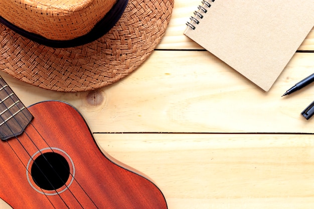 close-up ukulele and hat on wood background. over light