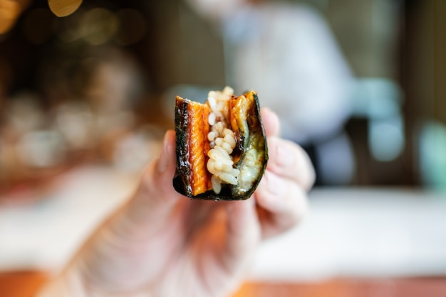 Close-up unagi (Japanse gegrilde paling) handbroodje met knapperig gegrild zeewier en sushirijst in de hand.