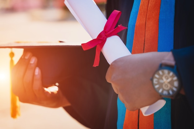 Close up of a university graduate holding degree certificate and mortarboard