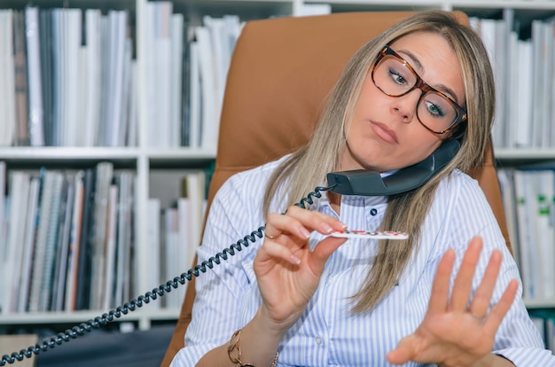 Close up of unmotivated blonde secretary polishing nails at workplace while talking on phone