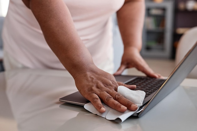 Close up of unrecognizable black woman cleaning laptop with sanitizing wipes copy space